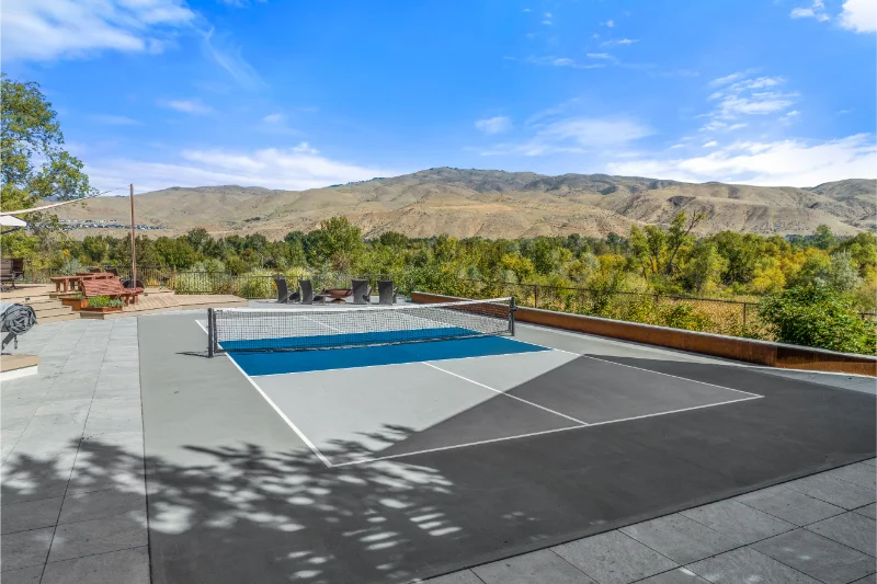 Pickleball court with mountain backdrop. Blue and gray court, net, trees, and sky.