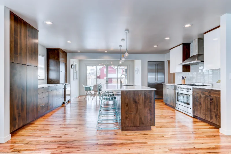 Modern kitchen with wood cabinets, island, and stainless steel appliances; light wood flooring.