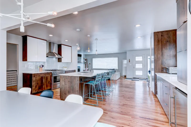 Modern kitchen and dining area with hardwood floors, white countertops, and wood cabinets.