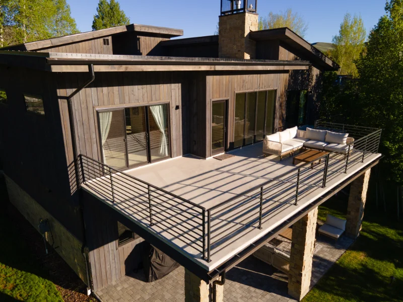 Modern home with a deck and patio, brown siding, a black railing, and outdoor furniture.