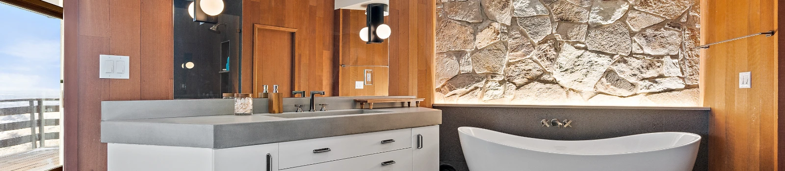 Bathroom with stone wall, wooden paneling, white vanity and tub, and decorative lights.