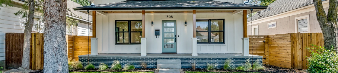 White-painted house with a porch and black-framed windows, and a turquoise door. Wooden fence to the sides.