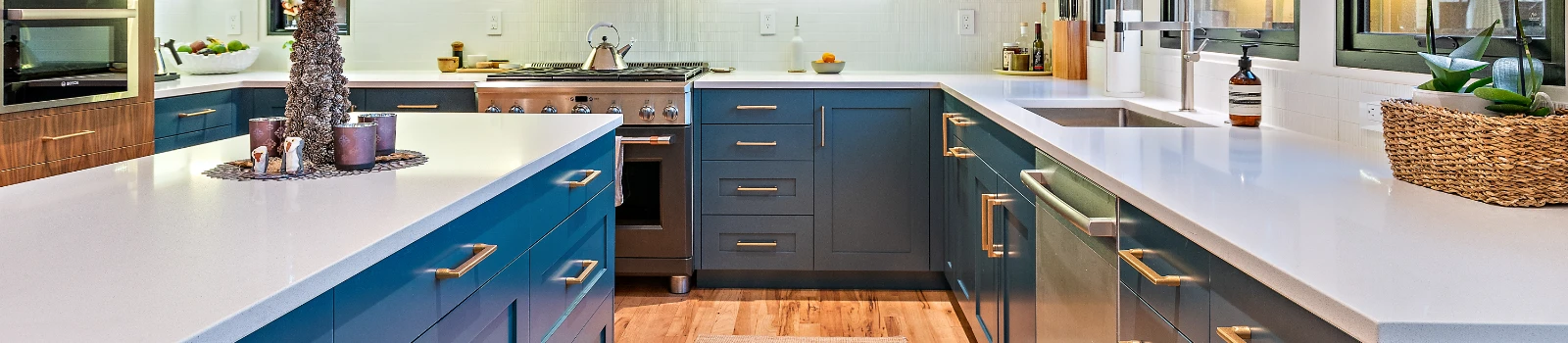 Modern kitchen with blue cabinets, white countertops, stainless steel appliances, and wood flooring.