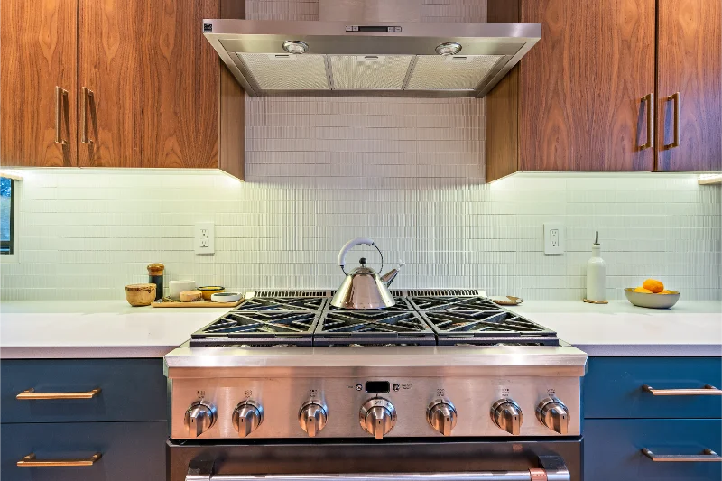 Modern kitchen with stainless steel range, teal cabinets, wooden upper cabinets, and white backsplash.