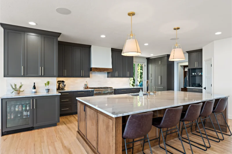 Modern kitchen with dark gray cabinets, light wood island, and pendant lights.