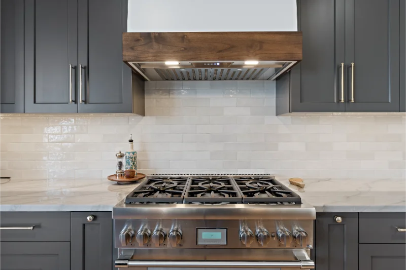 Kitchen with gray cabinets, stainless steel stove, and wooden range hood.
