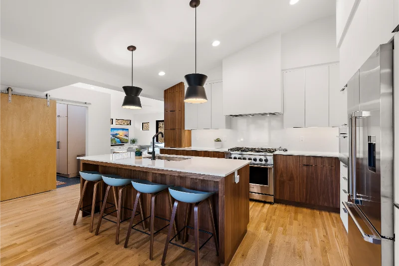 Modern kitchen with wood island, teal stools, stainless steel appliances, and pendant lights.