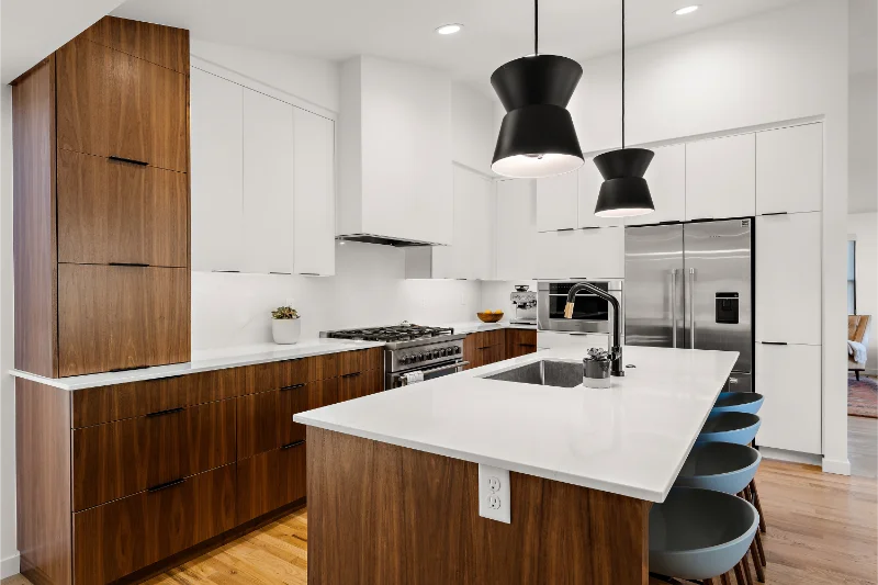 Modern kitchen with dark wood cabinets, white countertops, black pendant lights, and island with blue stools.