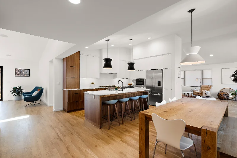 Open-plan kitchen and dining area with wood floors, island, and table. Modern, white walls and cabinetry; pendant lighting.
