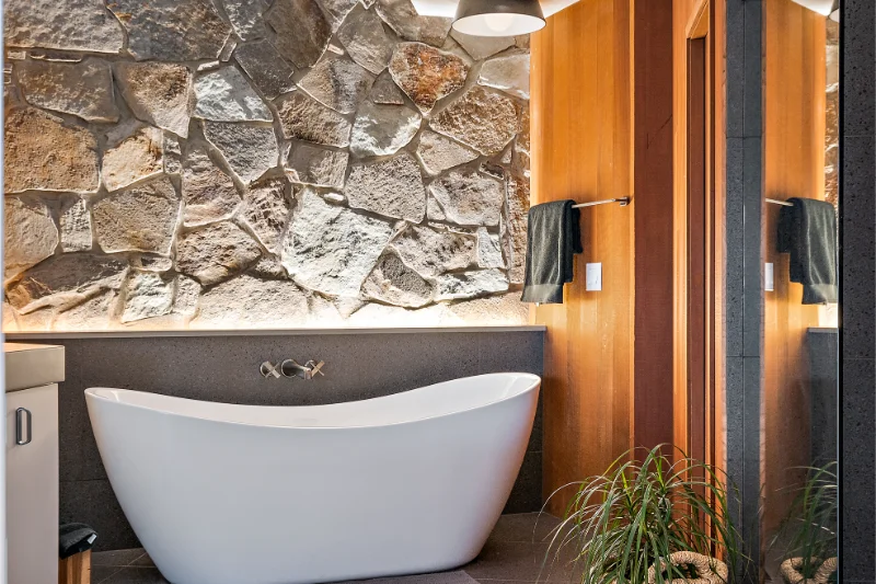 Bathroom with a white freestanding tub, stone wall, and wood accents.