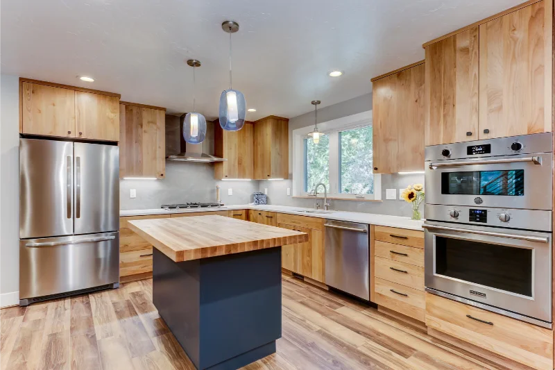 Modern kitchen with light wood cabinets, stainless steel appliances, and a blue island.