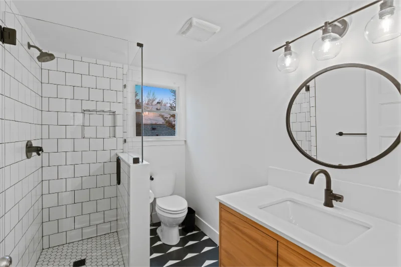 Modern white bathroom with subway tile shower, wood vanity, and black and white patterned floor.