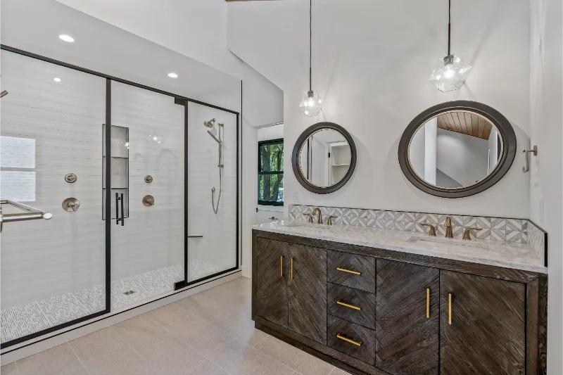 Modern bathroom with a glass shower, double vanity, and round mirrors.