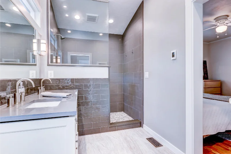 Bathroom with a white vanity, gray tiled shower, and a glimpse of a bedroom.