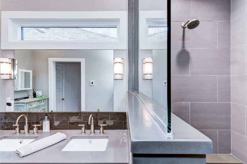 Modern bathroom with gray tile, double sinks, and glass shower divider.