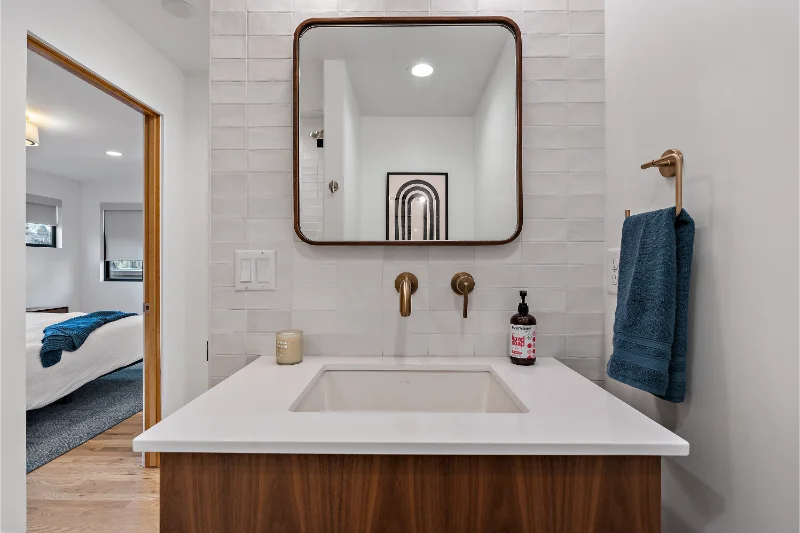 Modern bathroom with a brown vanity, square mirror, gold fixtures, and blue towel.