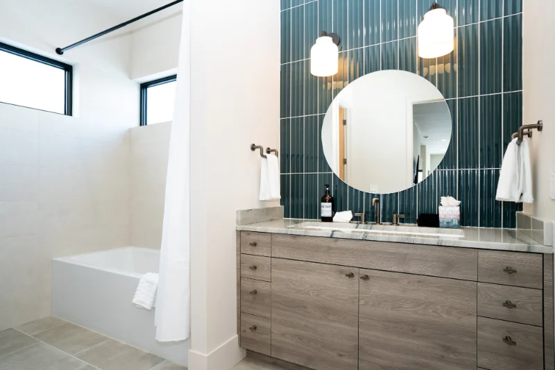 Bathroom with blue tile wall, round mirror, wood vanity, and a tub.
