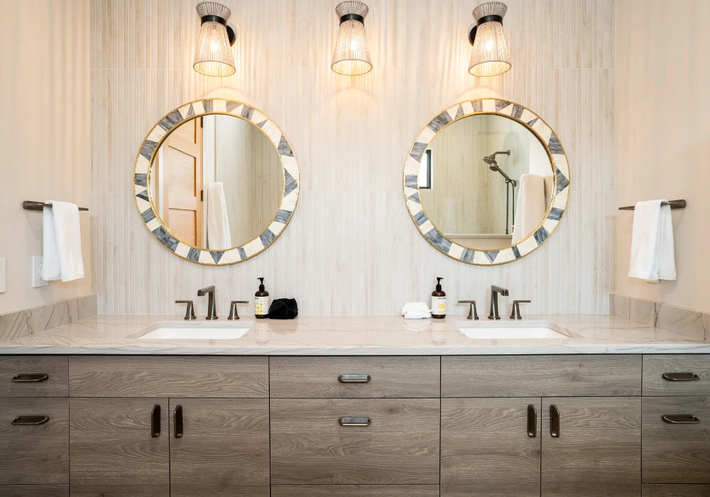 Double vanity bathroom with round mirrors and wood cabinets. Light fixtures above.
