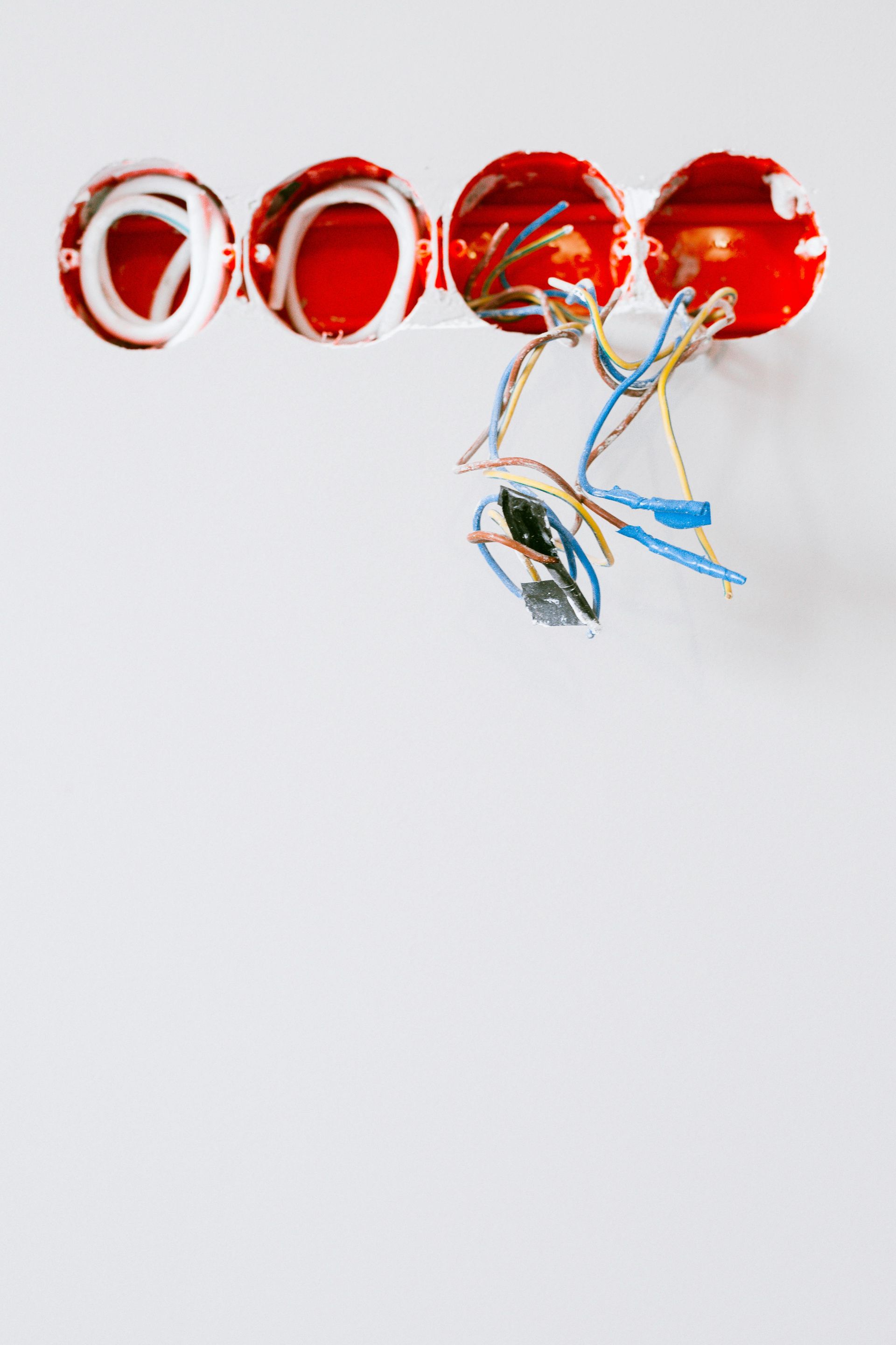 Four red circular electrical junction boxes embedded in a white wall with various exposed colored wires hanging out.