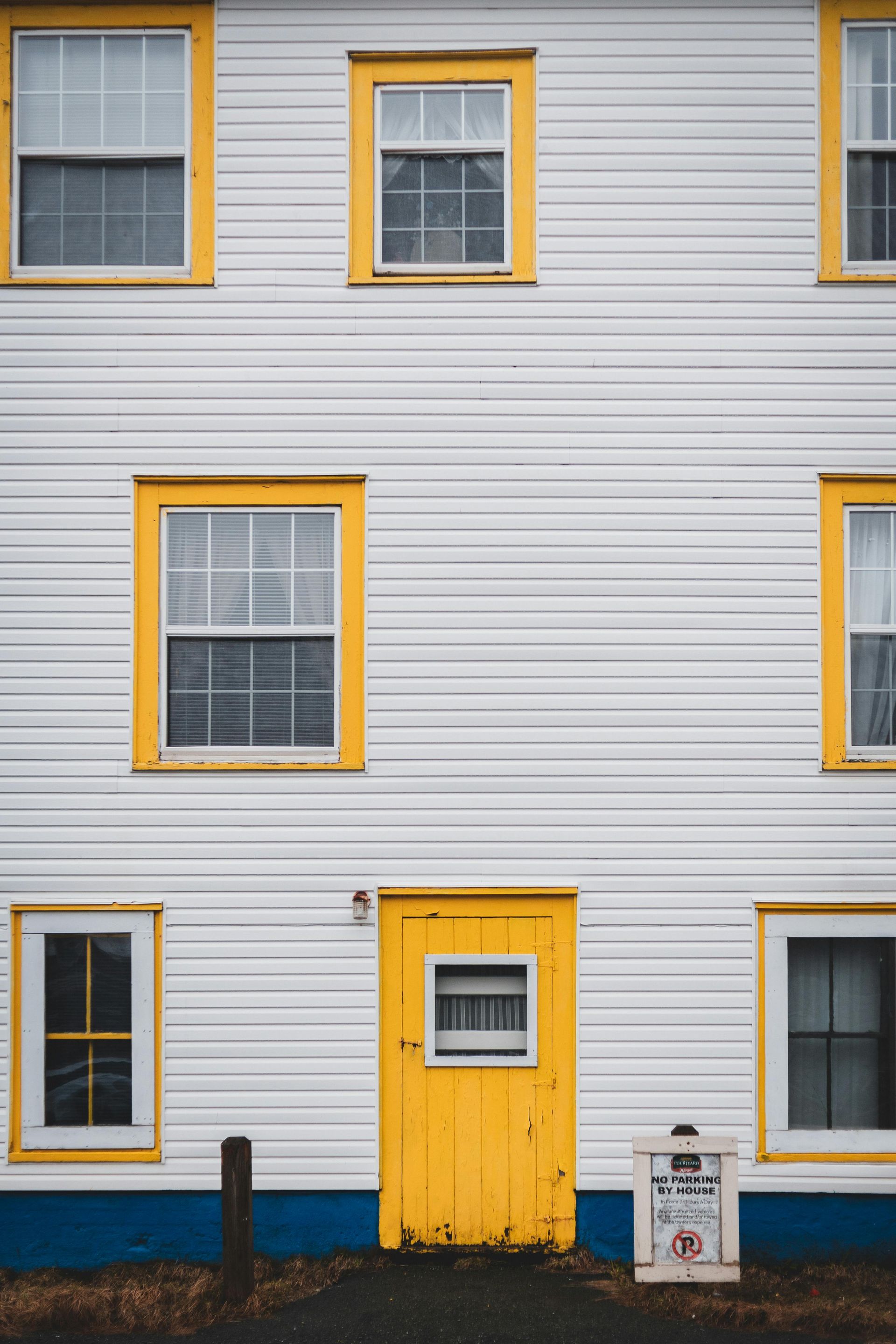 A white building with horizontal siding features a bright yellow door and several matching yellow-trimmed windows.