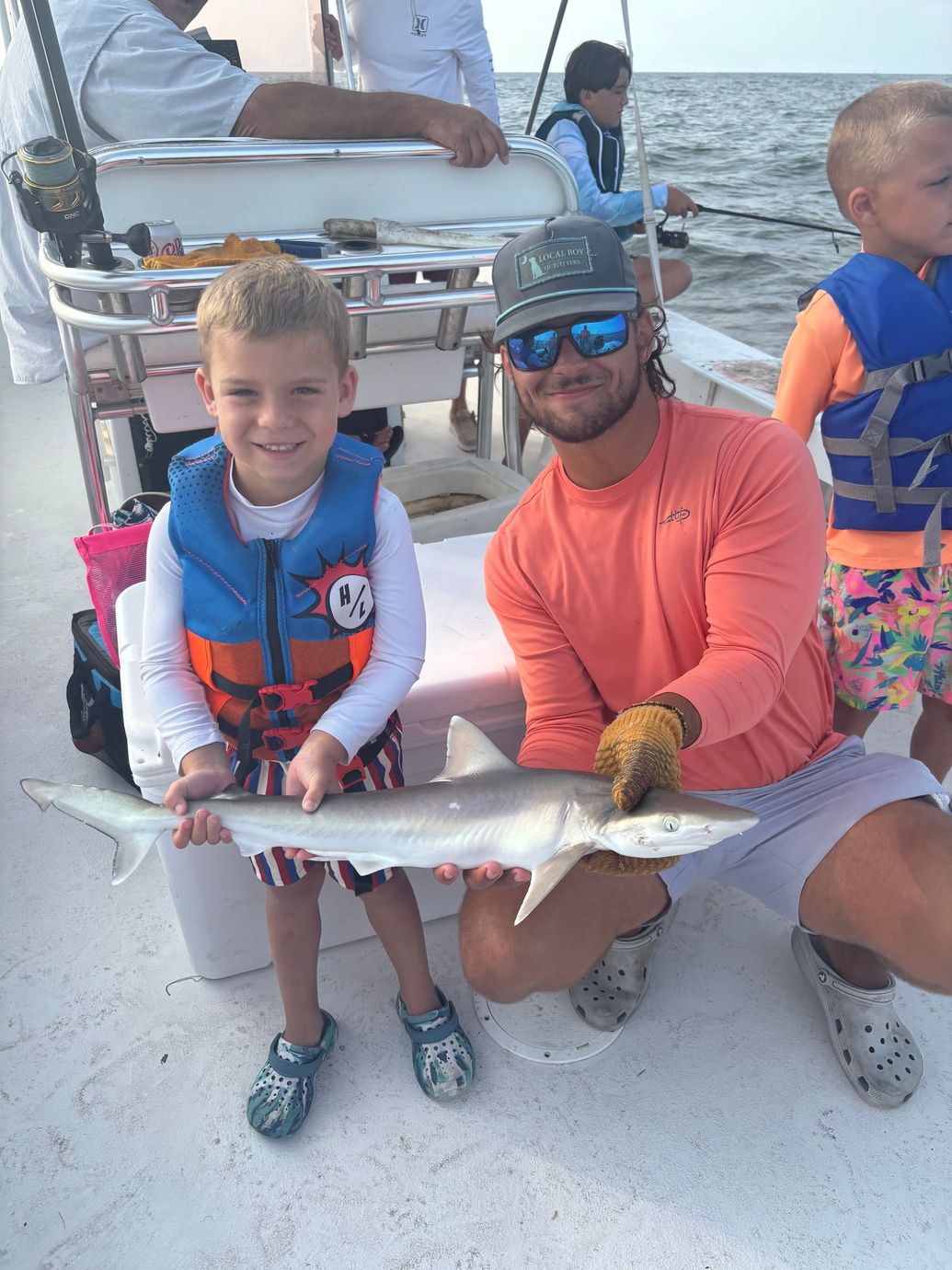 Three young boys are standing next to a shark on a boat.
