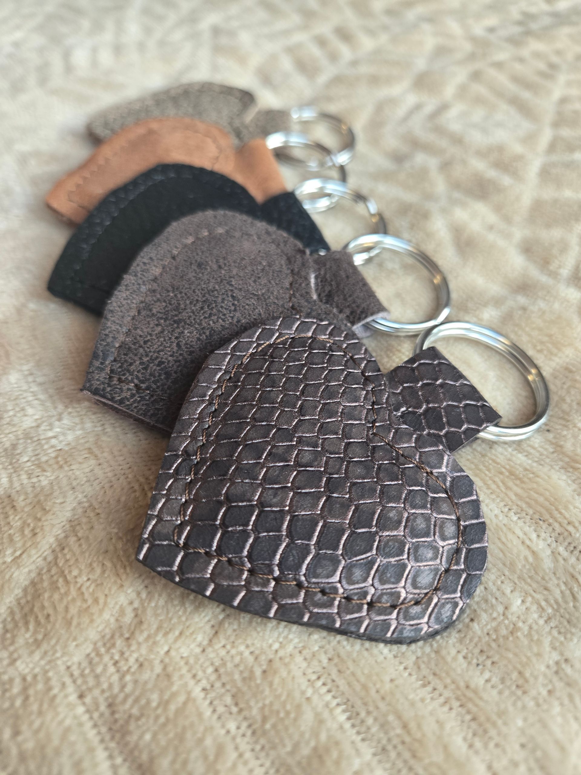 Vijf hartvormige leren sleutelhangers op een rij, met verschillende texturen en kleuren, gerangschikt op een stoffen ondergrond.