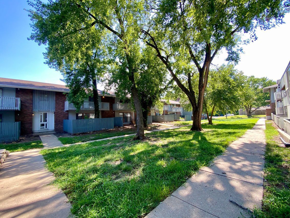 Apartment complex with trees and green grass on a sunny day. Concrete walkways.