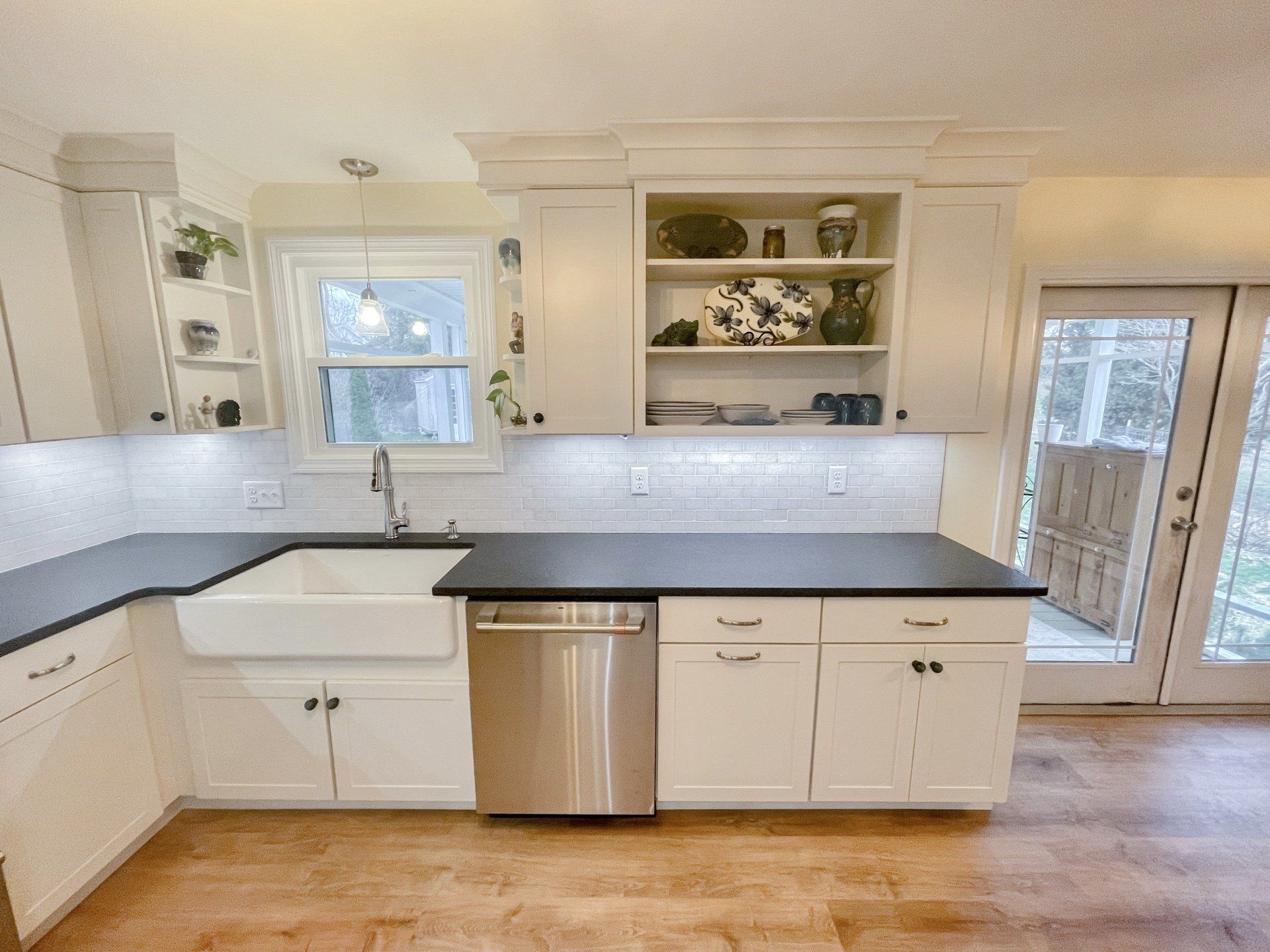 A kitchen with white cabinets , black counter tops , a sink and a stainless steel dishwasher.