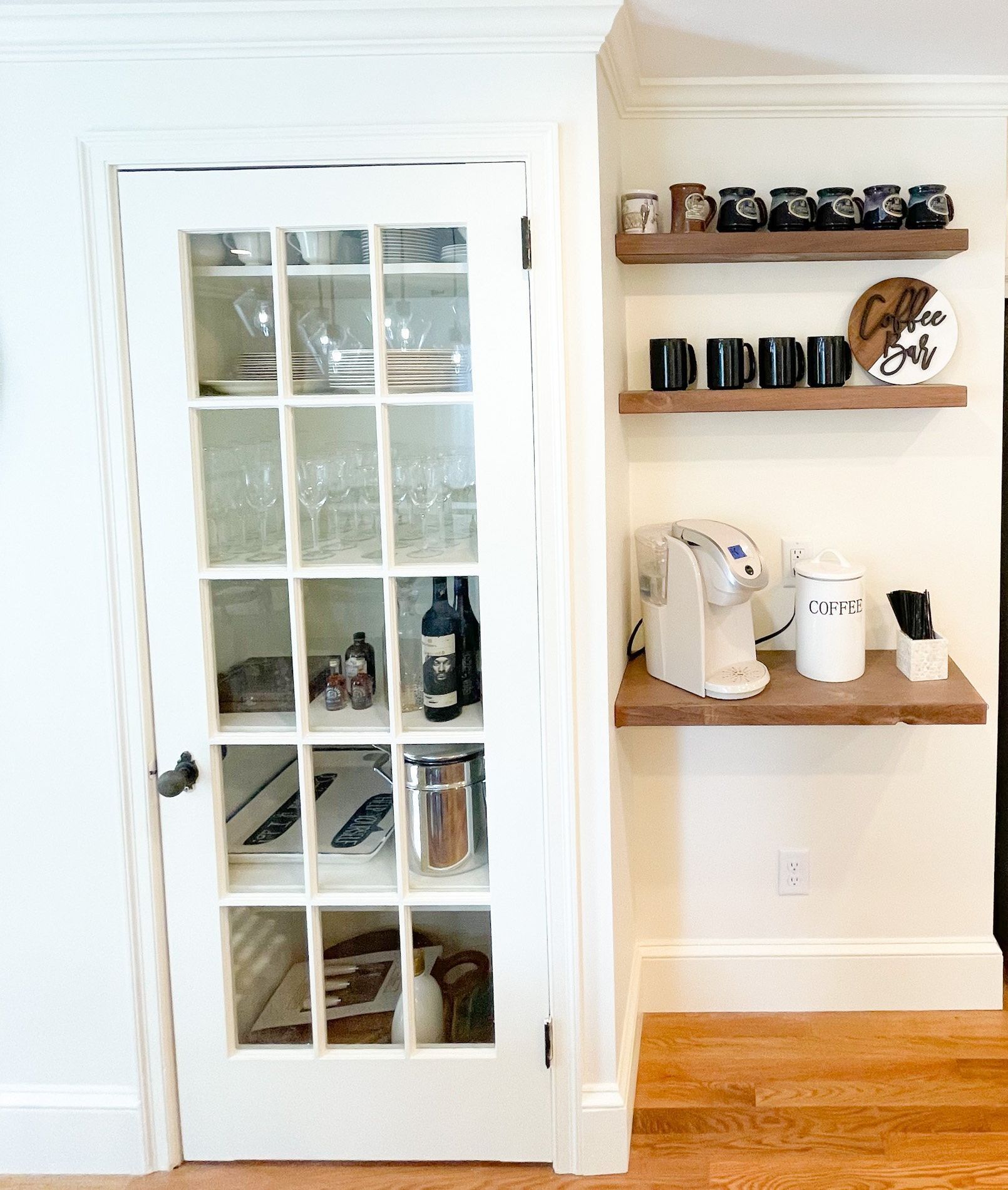 A kitchen with a glass door , shelves , and a coffee maker.
