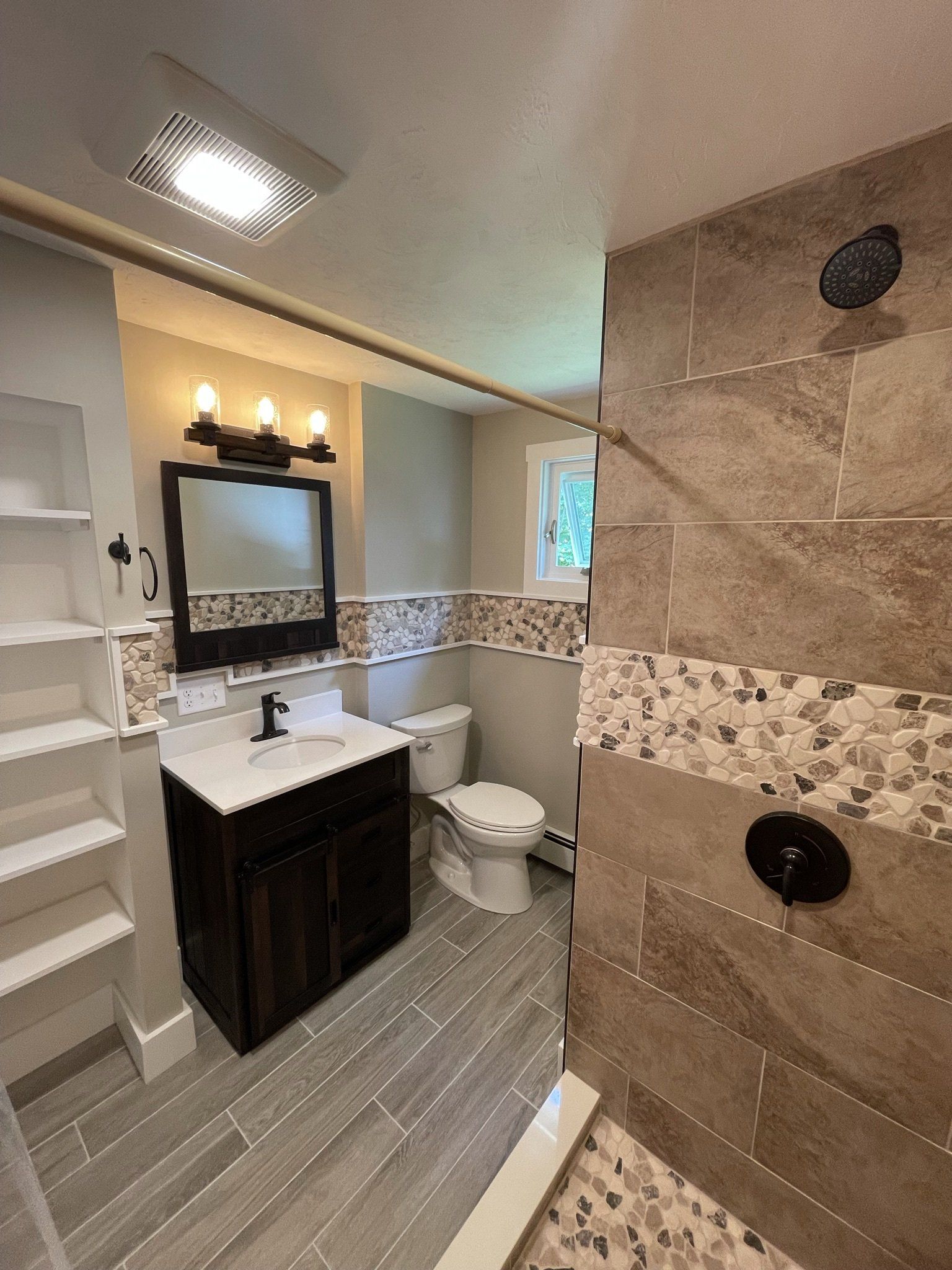 A bathroom with a sink , toilet , shower and mirror.