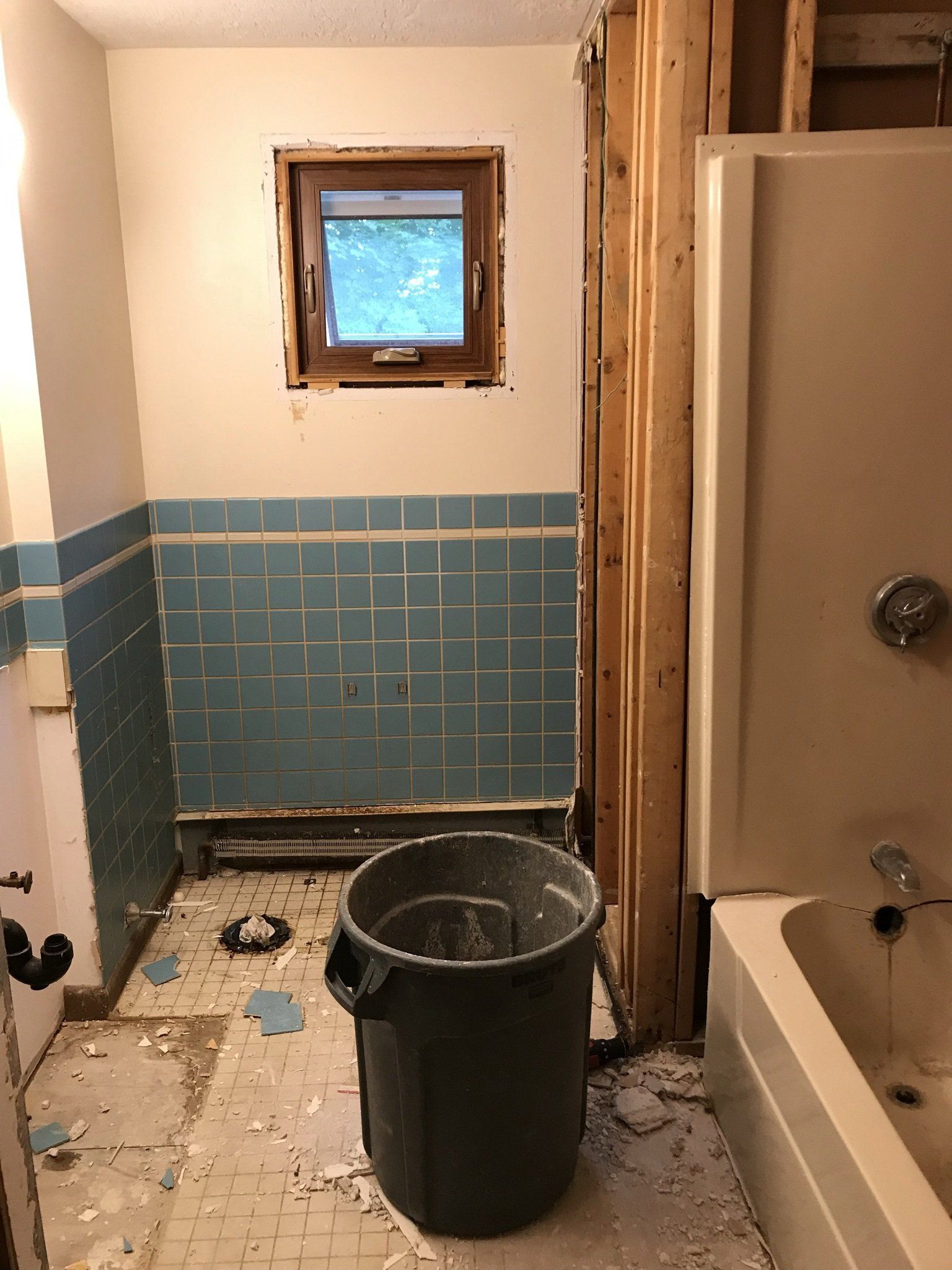 A bathroom with blue tiles and a trash can on the floor.