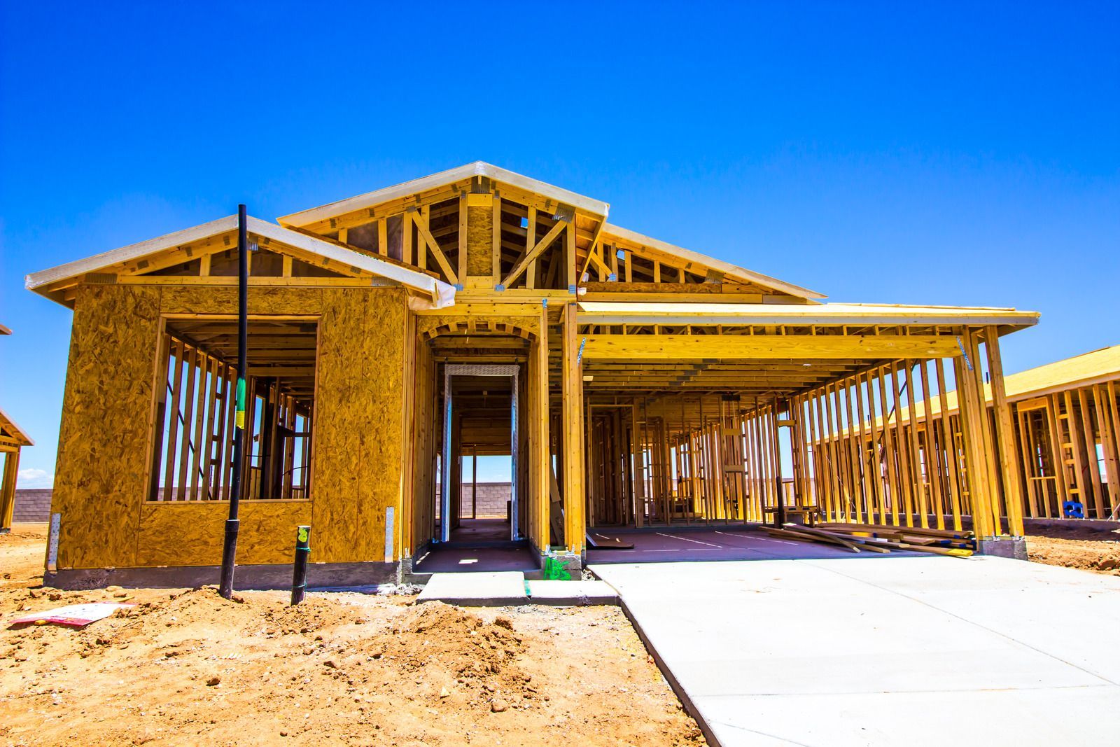 Framed wooden structure of a house under construction; bright blue sky overhead.