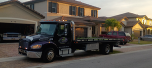 Black flatbed tow truck parked on a suburban street in front of houses at sunset