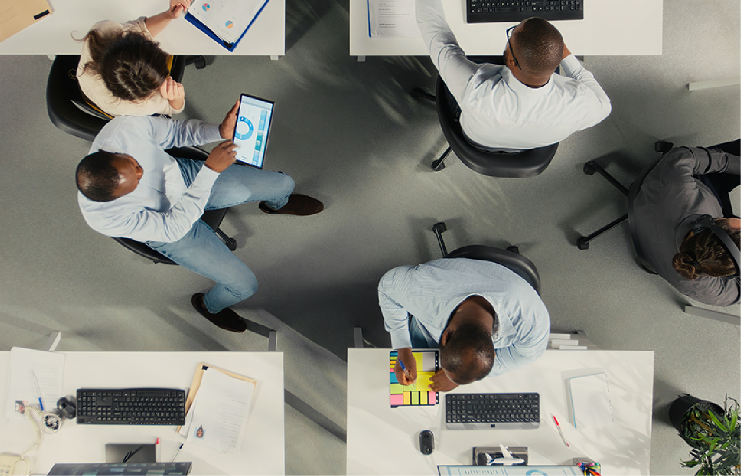 Top-down view of people working at desks in a modern office, collaborating on projects using computers and tablets.