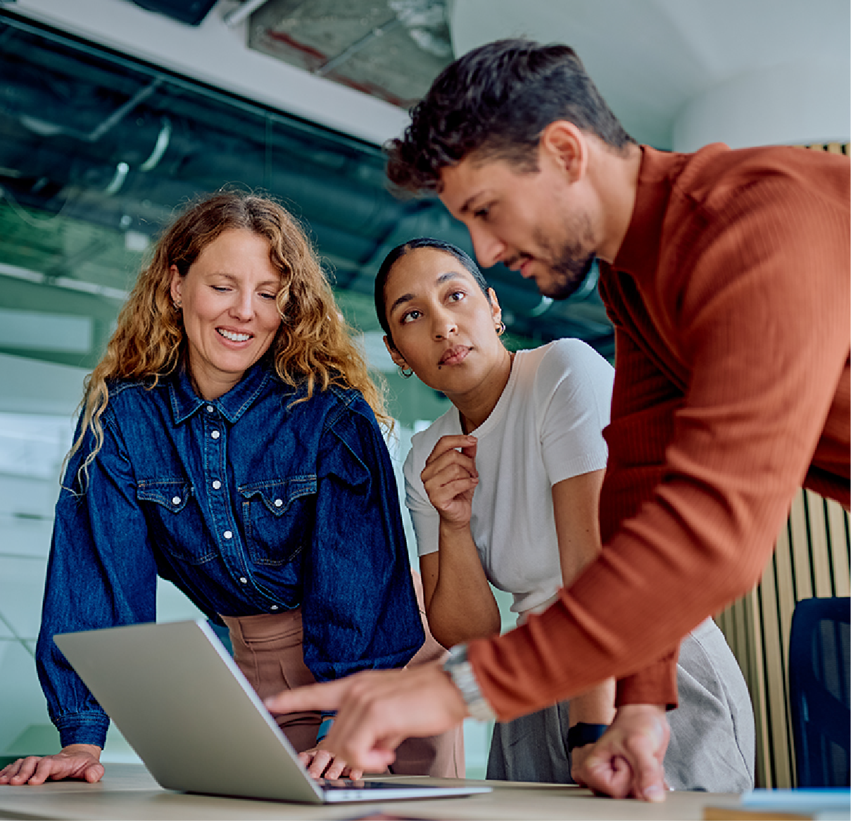 Three colleagues look at a laptop screen during a meeting in a bright office.
