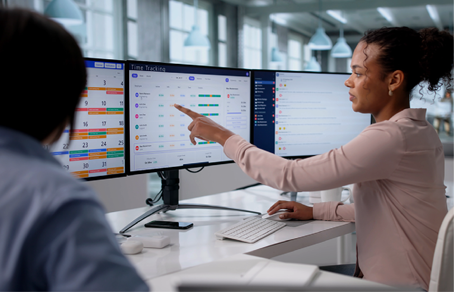 Two professionals looking at computer monitors in an office, one pointing at data on a screen.