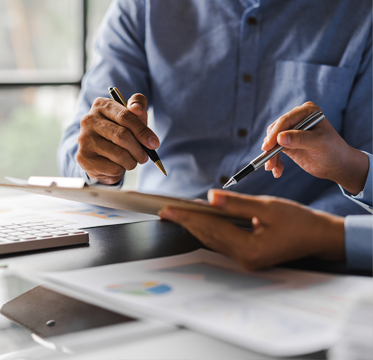 Two people work together at a desk, pointing with pens at documents and charts during a professional consultation.