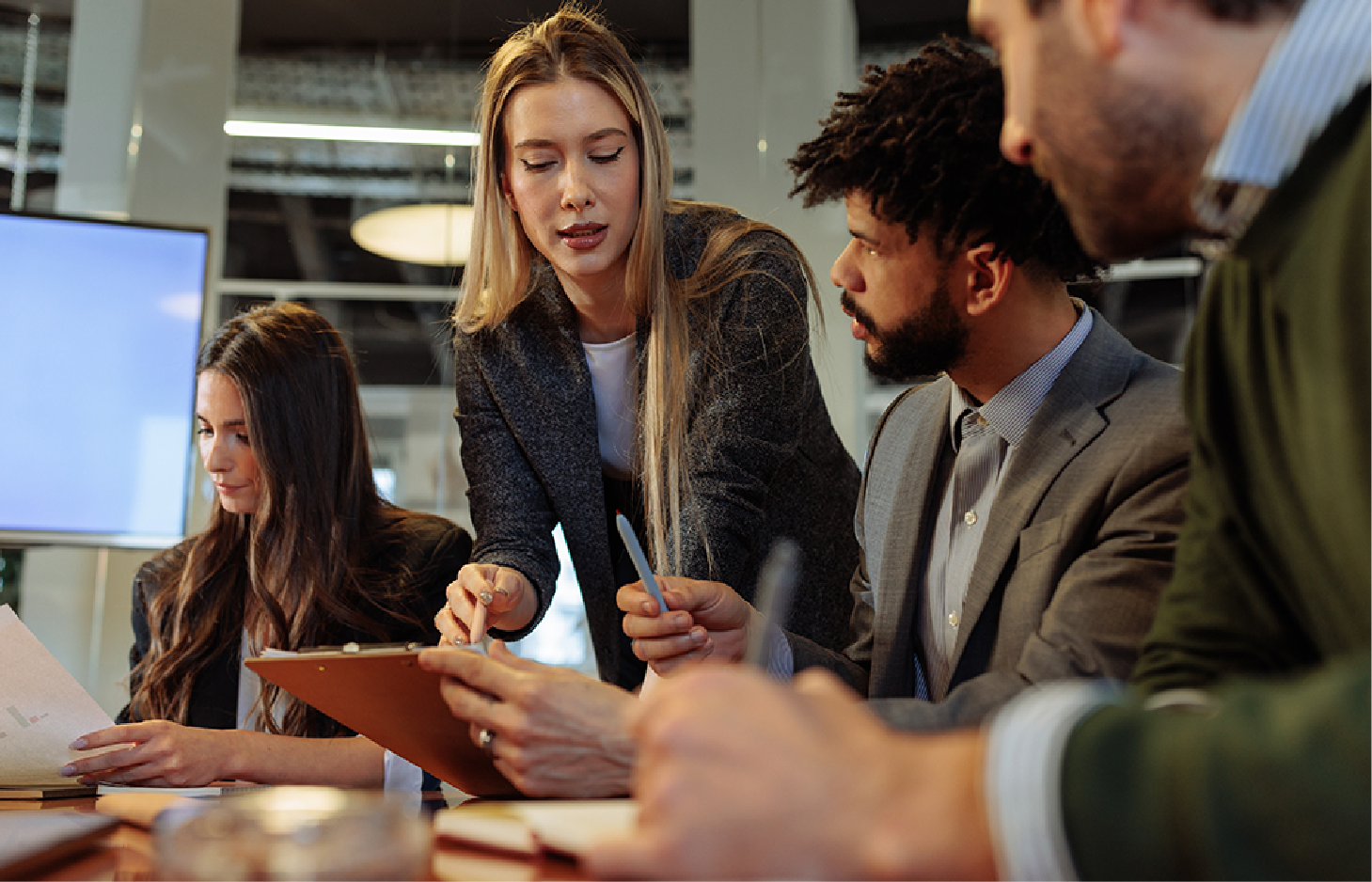Four professionals collaborate at a table, reviewing documents and discussing work in a modern office setting.