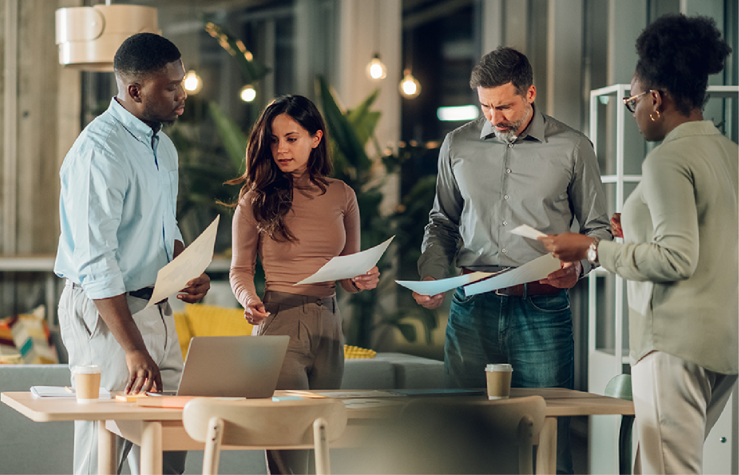 A professional team works together around a table in a modern, well-lit office, reviewing documents and a laptop.