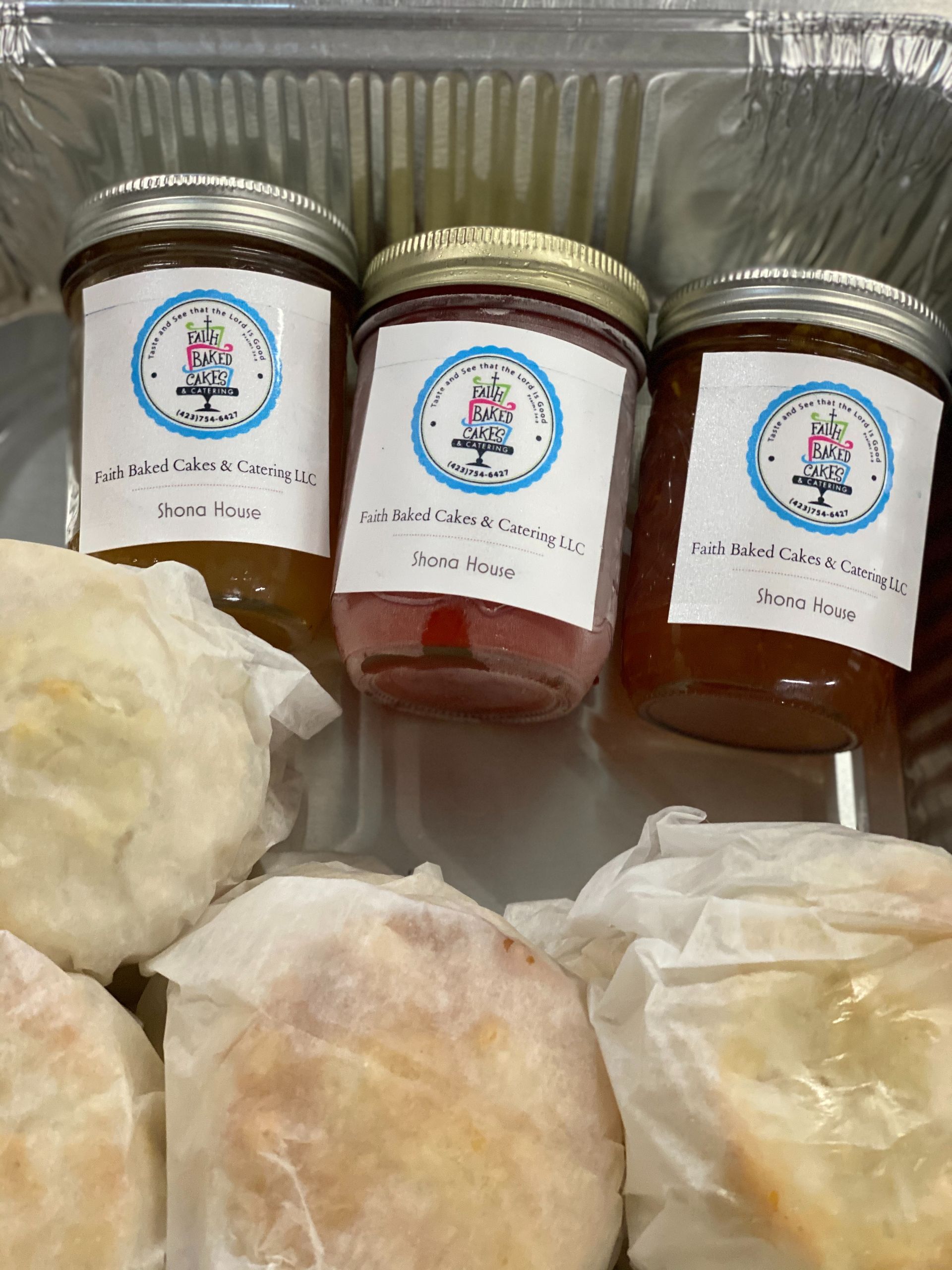Three jars of preserves in a box with several wrapped bread rolls or pastries