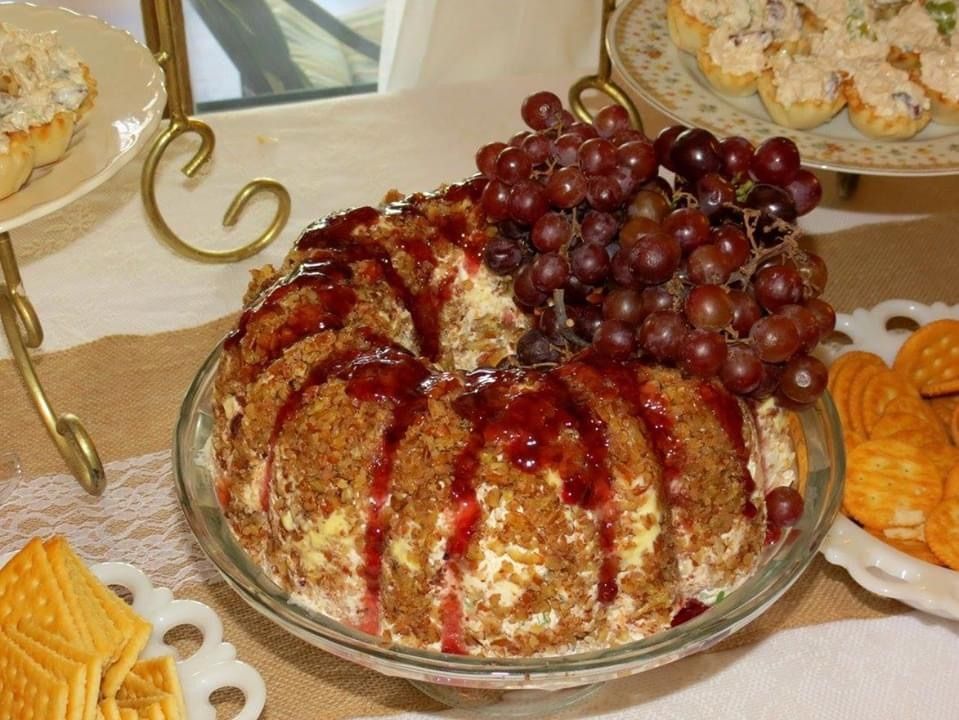 Festive bundt cake topped with grapes and red glaze on a table with other desserts