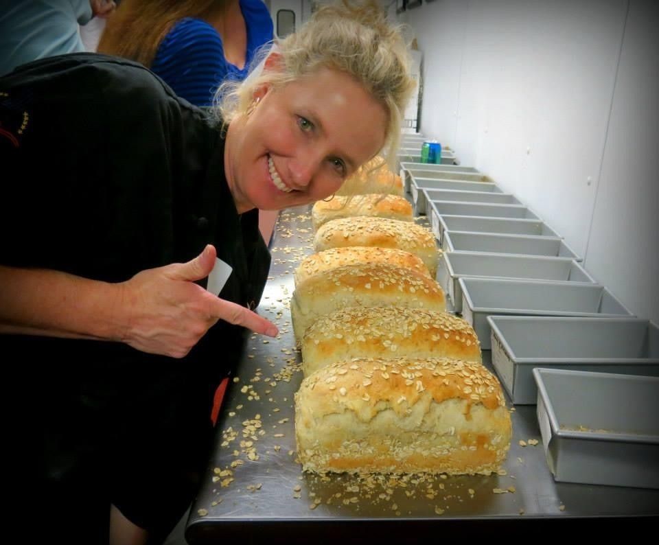 Woman points to rows of loaves on a conveyor line in a bakery kitchen.