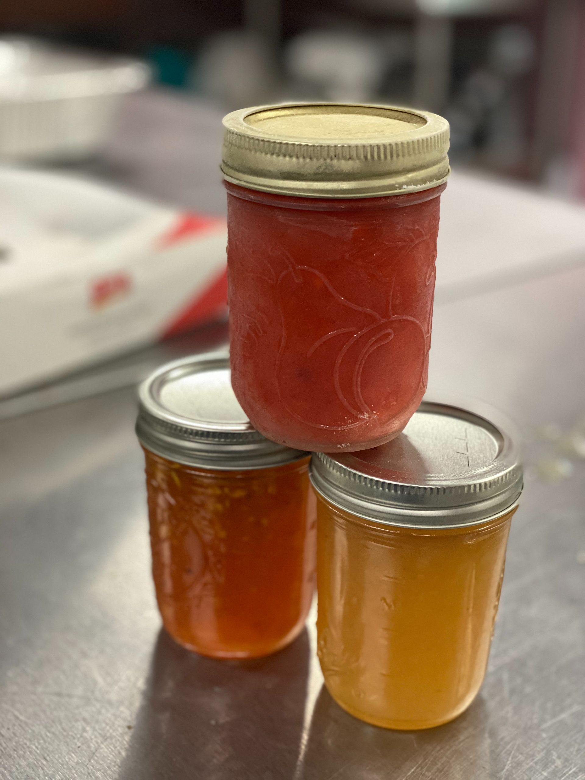 Three small jars of amber and red preserves stacked on a table.
