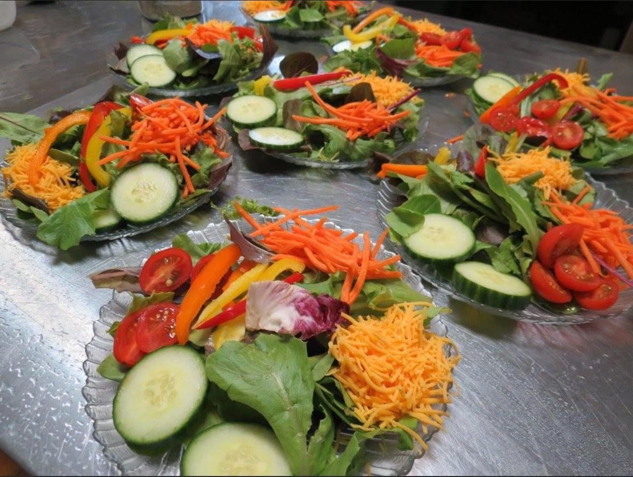 Assorted vegetable salads with cucumbers, carrots, tomatoes and greens arranged on a stainless steel table
