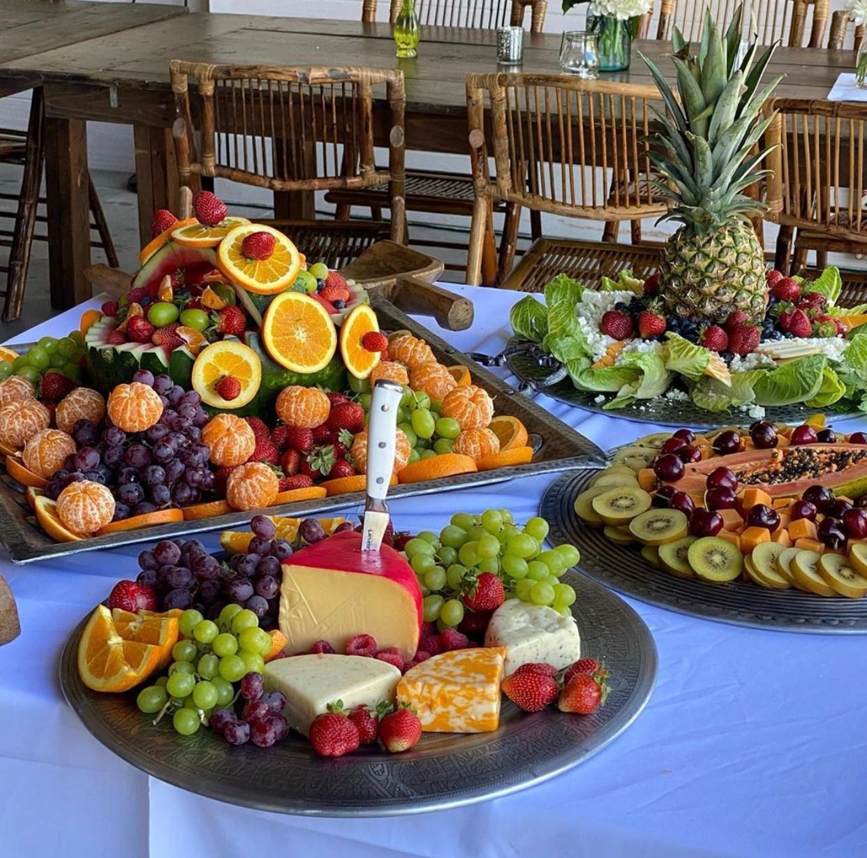Fruit platters on a table with pineapple, kiwi, grapes, oranges, and melon slices at a buffet.