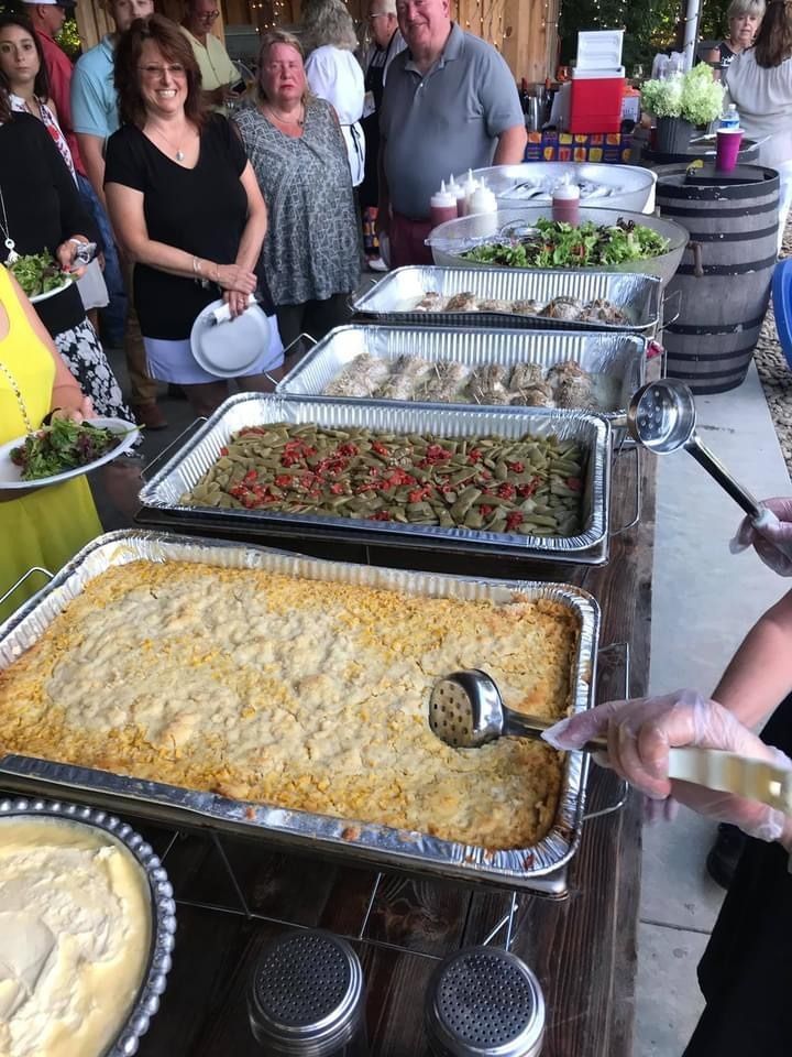 Buffet table with casseroles and salad while people stand nearby at an indoor gathering