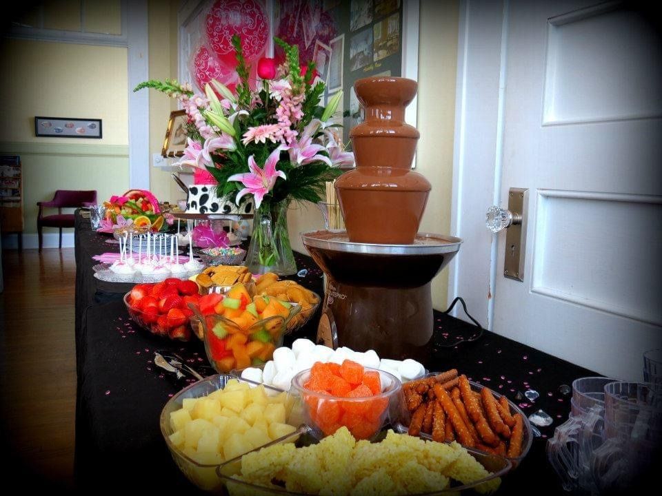 Dessert buffet with fruit, cookies, and a chocolate fountain on a decorated table
