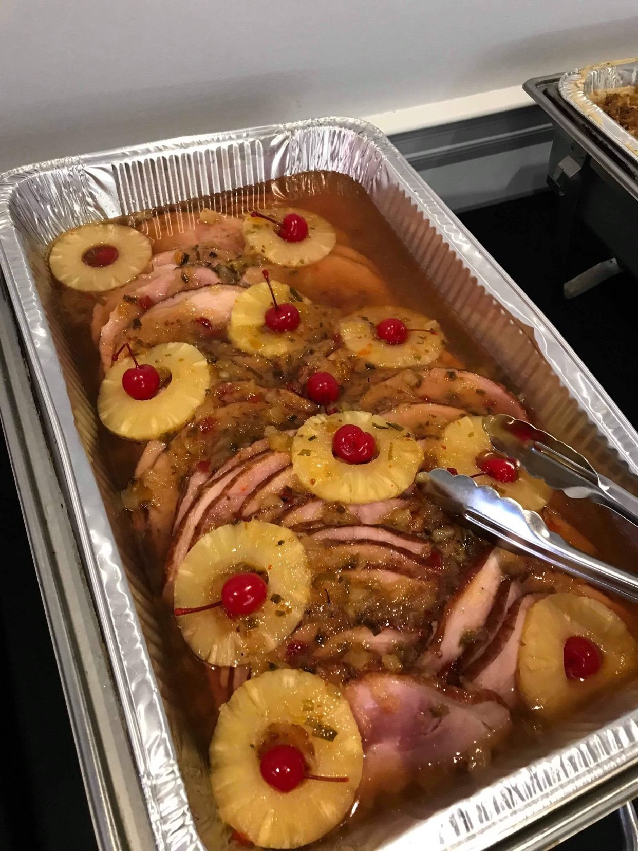 Baked ham in a foil tray topped with pineapple rings and maraschino cherries