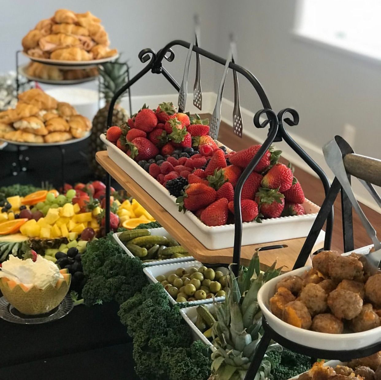 Elegant buffet table with fresh strawberries, fruit, pastries, and fried snacks in black serving stands