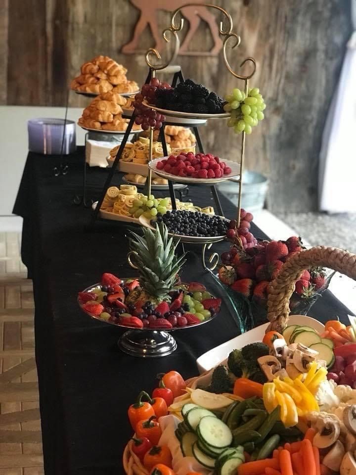 Tiered fruit display on a black table with grapes, strawberries, pineapple, and sliced vegetables at a buffet.